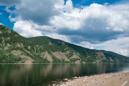 A Green Mountain Near the Body of Water Under the Blue Sky and White Clouds