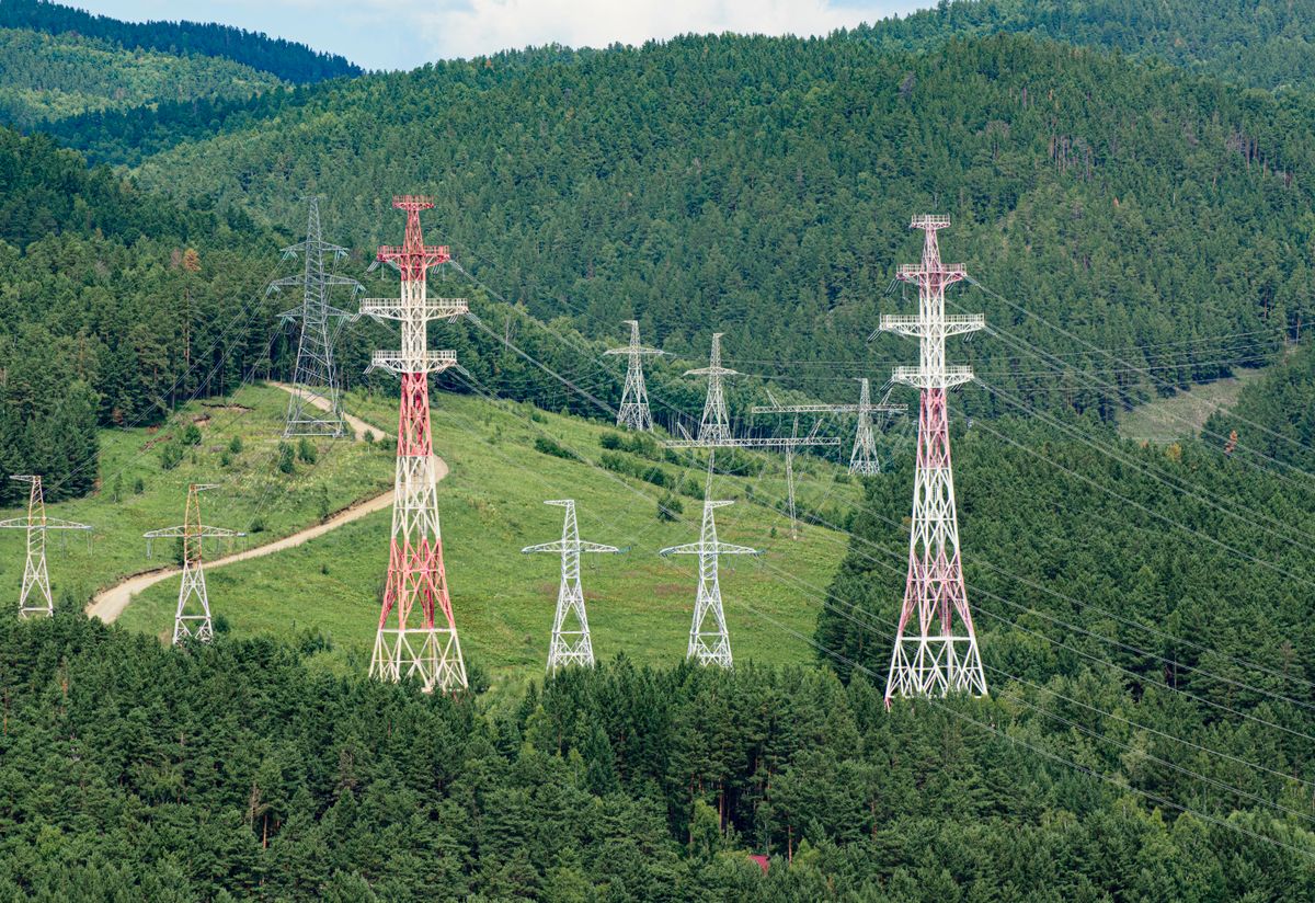 High-voltage transmission towers stretching through forested hills, the interconnected system that carries Interchange between Balancing Authority Areas