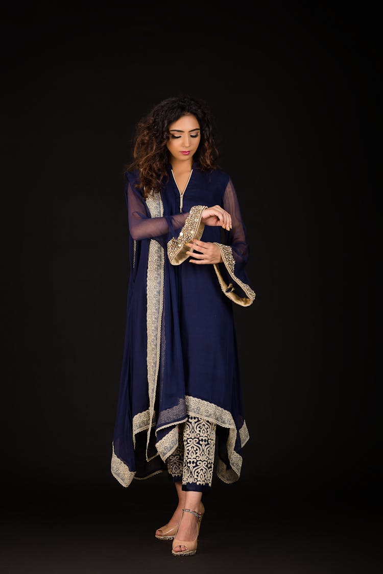 Woman Wearing Navy Blue Dress With Golden Sequins Standing Against Black Background