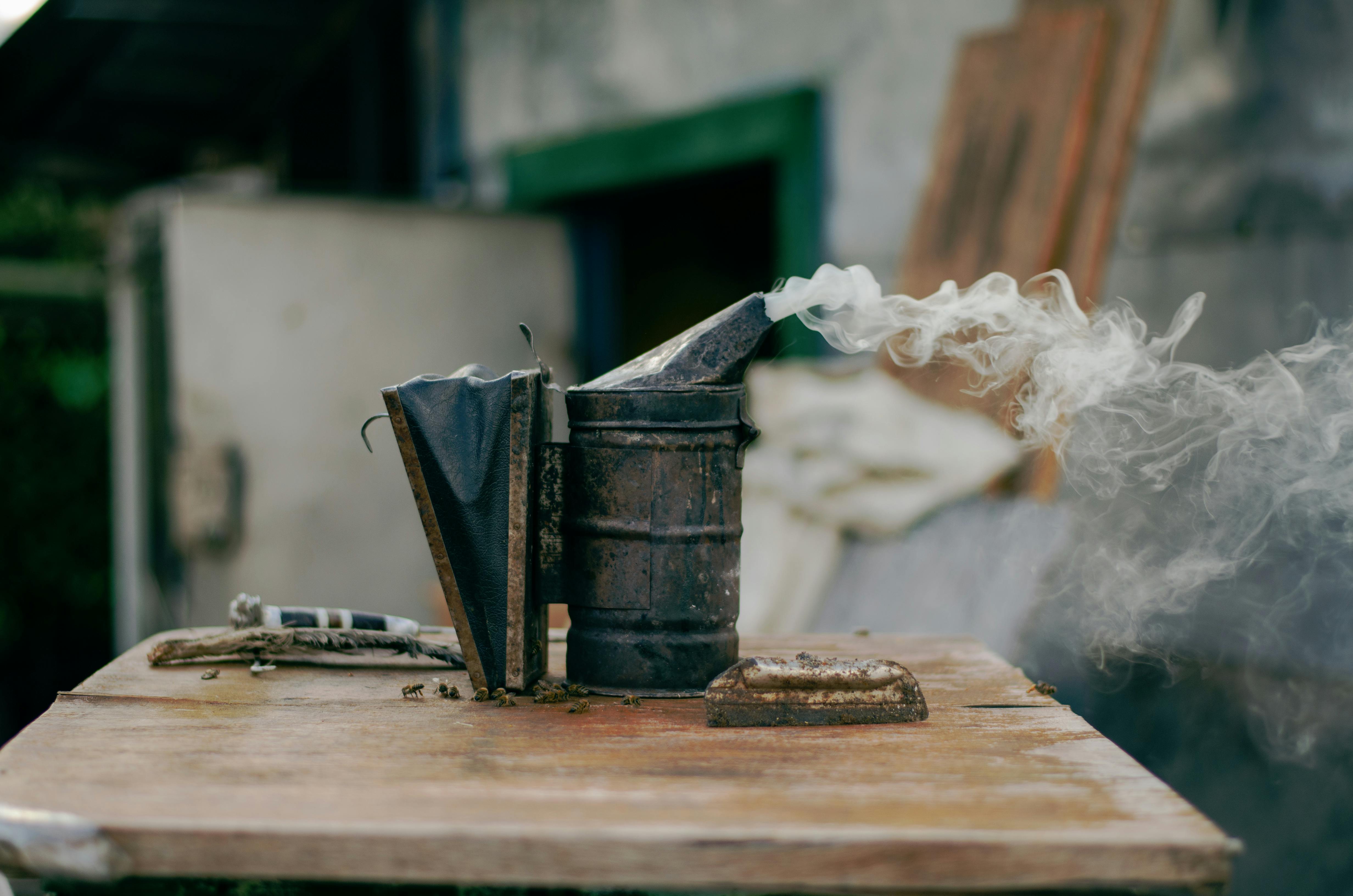 Close-up of a bee smoker releasing smoke on a wooden surface, outdoors.