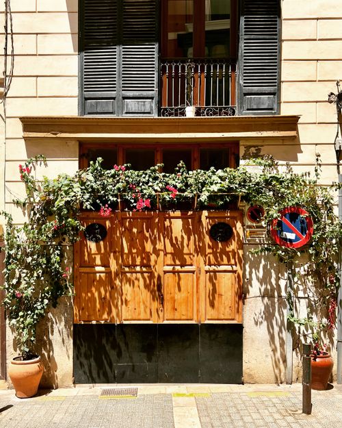 Free Mediterranean style facade with wooden doors, balcony and climbing plants in sunlight. Stock Photo