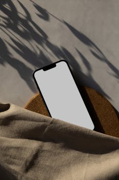 A smartphone with a blank screen in a minimalist setting, featuring dramatic shadows.