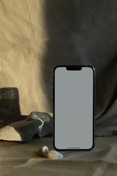 Smartphone with blank screen and seashells on a textured fabric background.