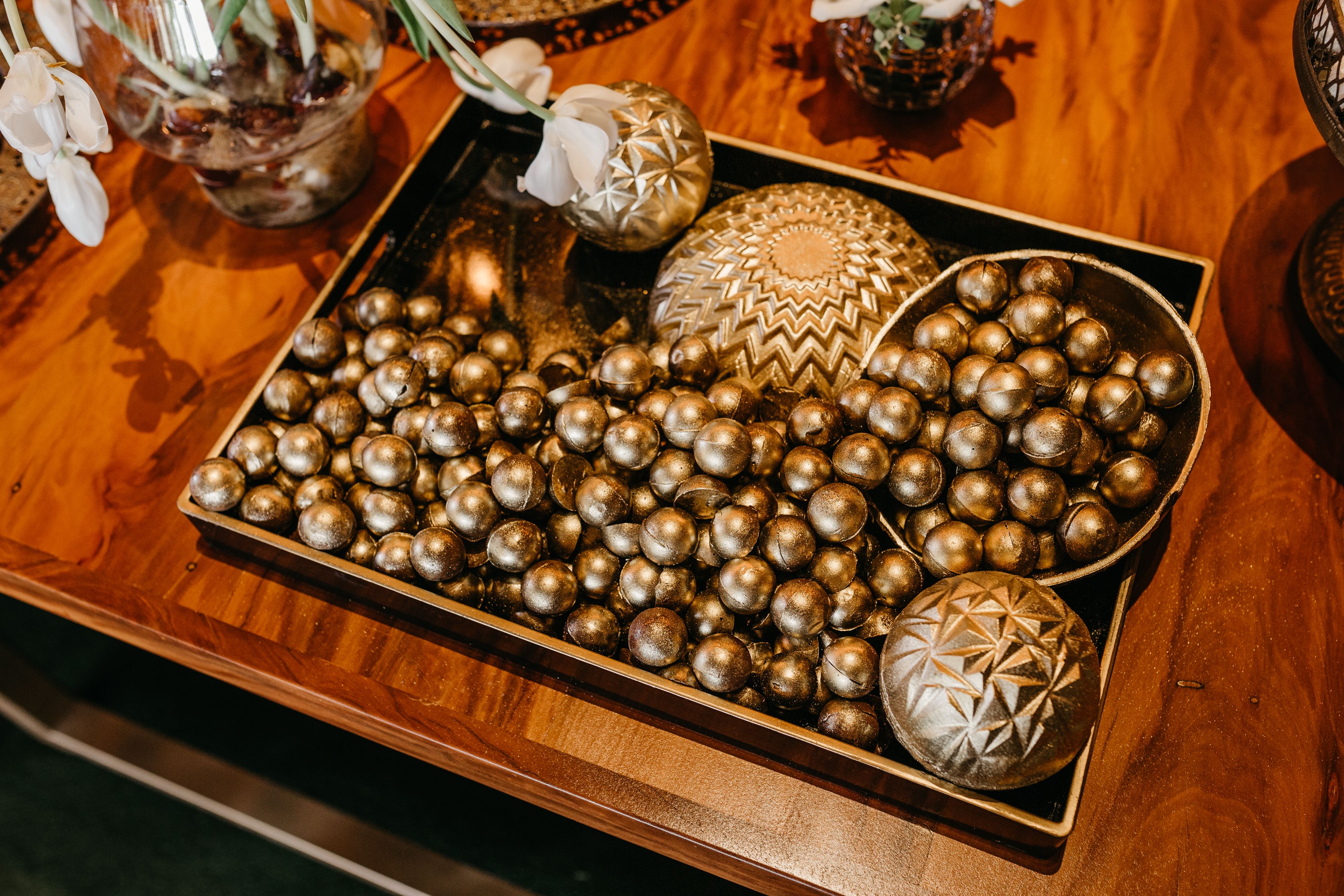 A beautiful arrangement of golden decorative balls in a wooden tray with floral accents, perfect for home decor.