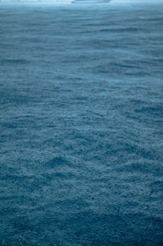 Peaceful scene capturing raindrops falling on a vast expanse of blue ocean waters, evoking calmness and serenity.