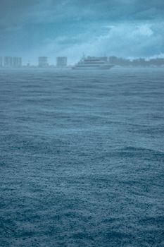 Dramatic seascape capturing a ship silhouette on a rainy day with city skyline in the background.