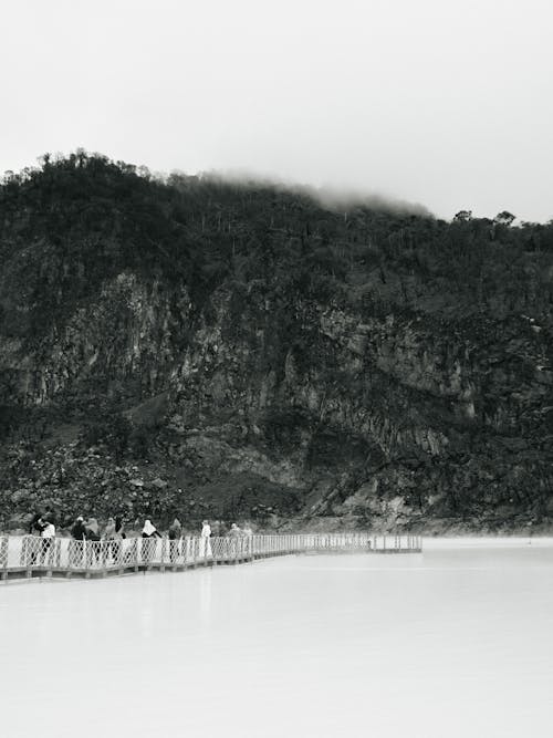 Grayscale Photo of People Walking Under the Rock Mountains 