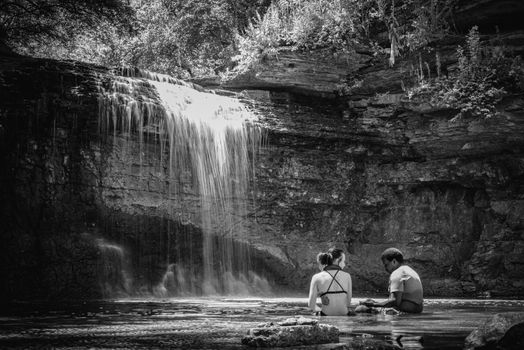 Couple enjoying peaceful time by a waterfall, expressing unity and nature's beauty.