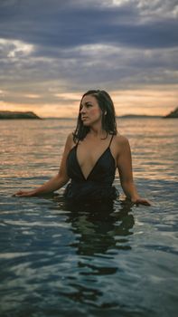 A woman in a black swimsuit stands in shallow water during a picturesque sunset at Rosario Beach.
