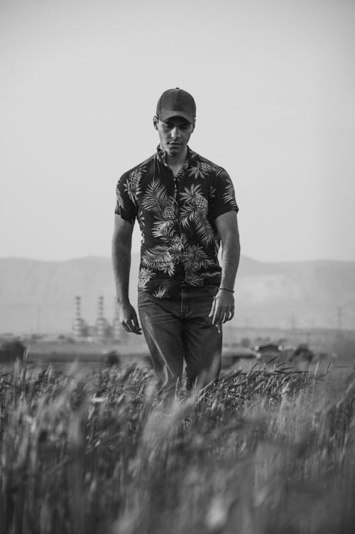 Grayscale Photo of a Man Wearing Aloha Shirt while Walking on Grass Field