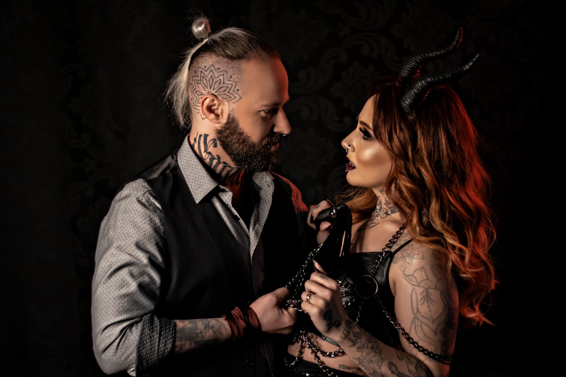 Couple posing in dark fashion with tattoos and devil horns, showcasing edgy style.