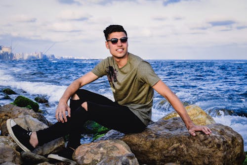 Man Sitting on Rock Near Body of Water