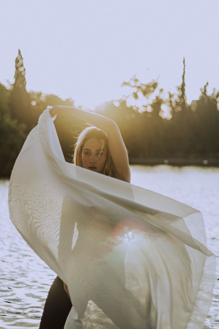 Woman Posing With White Veil By Lake Shore