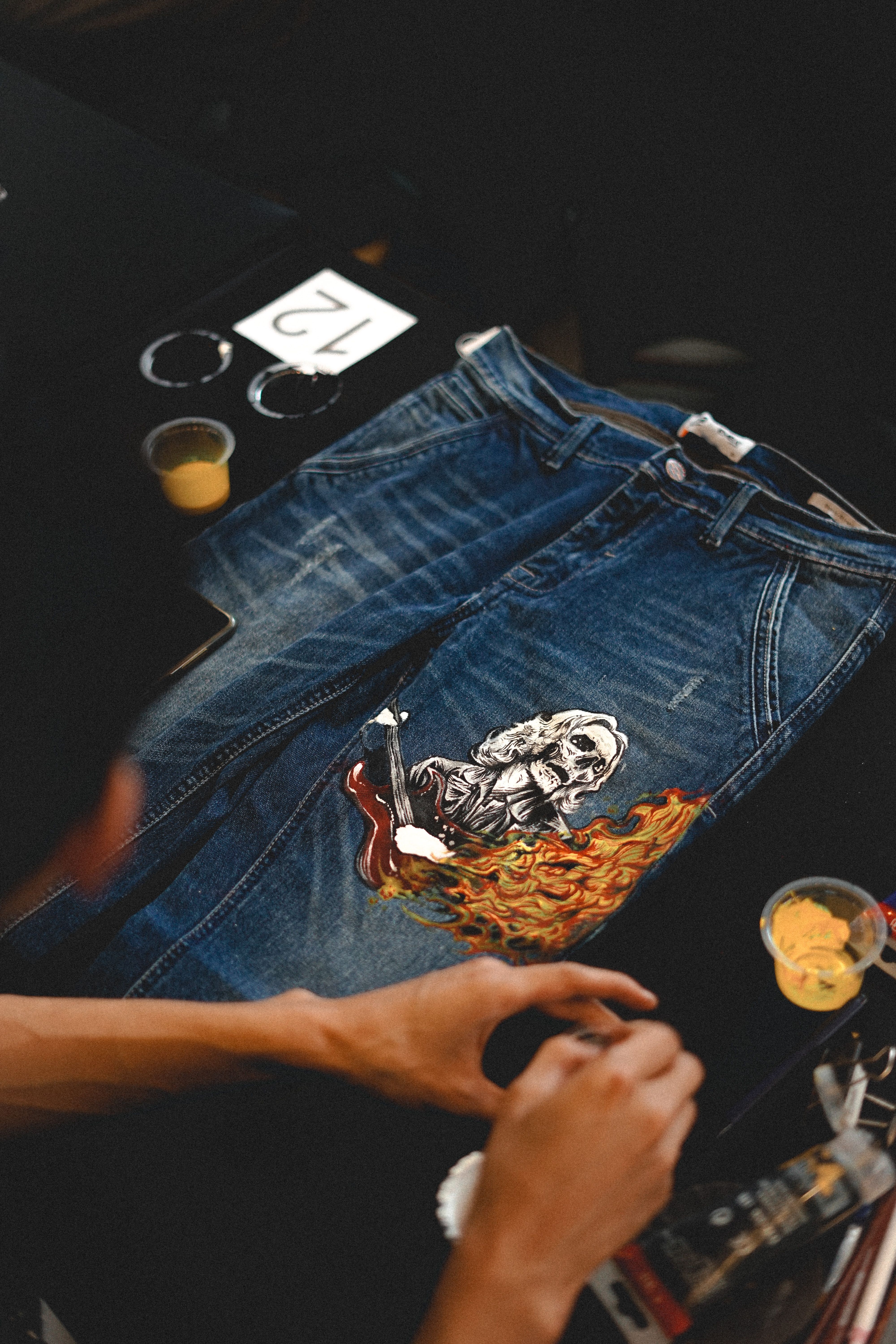 Close-up of artist painting a unique design on blue denim jeans with vibrant colors.