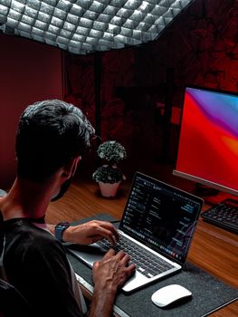A man working on a laptop in a modern and stylish indoor workspace with ambient lighting.