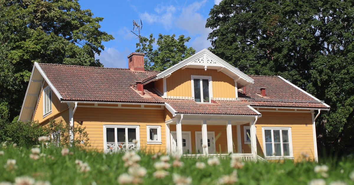 A picturesque yellow bungalow with a tiled roof surrounded by lush greenery under a bright blue sky.