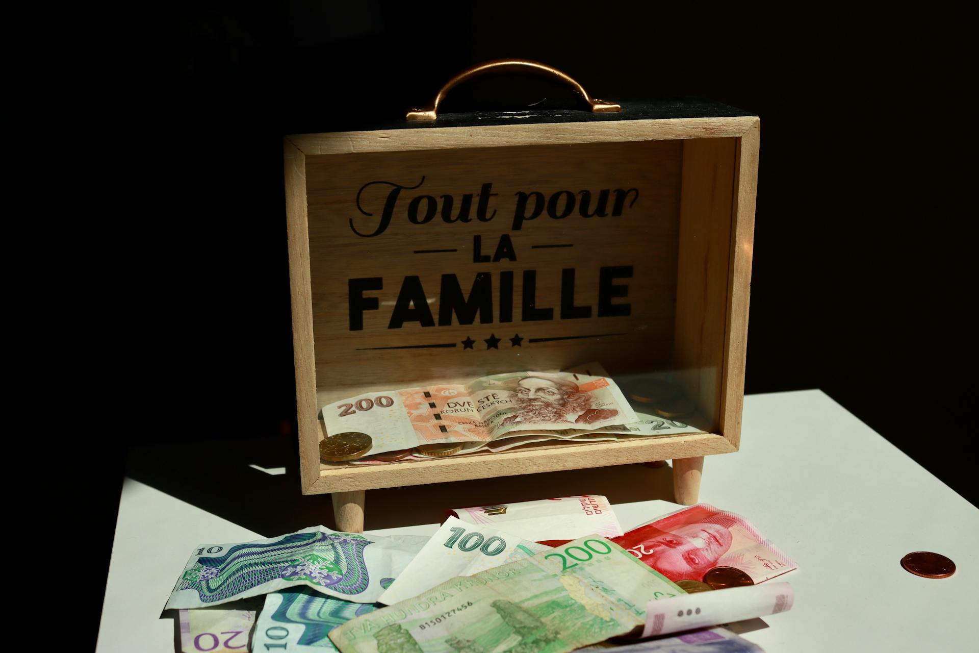 A wooden box with money and 'Tout pour la Famille' text, symbolizing family savings.