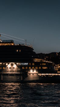 A grand cruise ship illuminated under a twilight sky, sailing on calm waters.