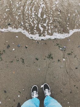 Feet in sneakers standing on sandy Vancouver beach near the shoreline.
