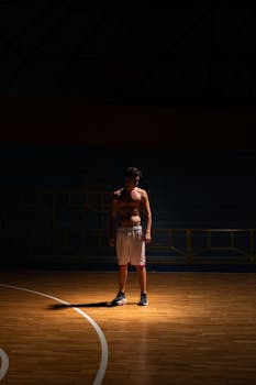 Dramatic shot of a shirtless athlete standing on a dimly lit basketball court.