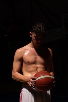 Intense low-light portrait of a shirtless basketball player holding a ball.