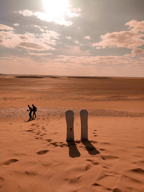 Free Persons Walking Near a Pair of Sandboards on Desert Stock Photo