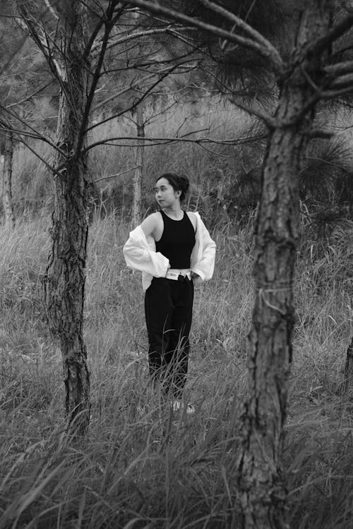 Woman Standing on Grass Between Bare Trees