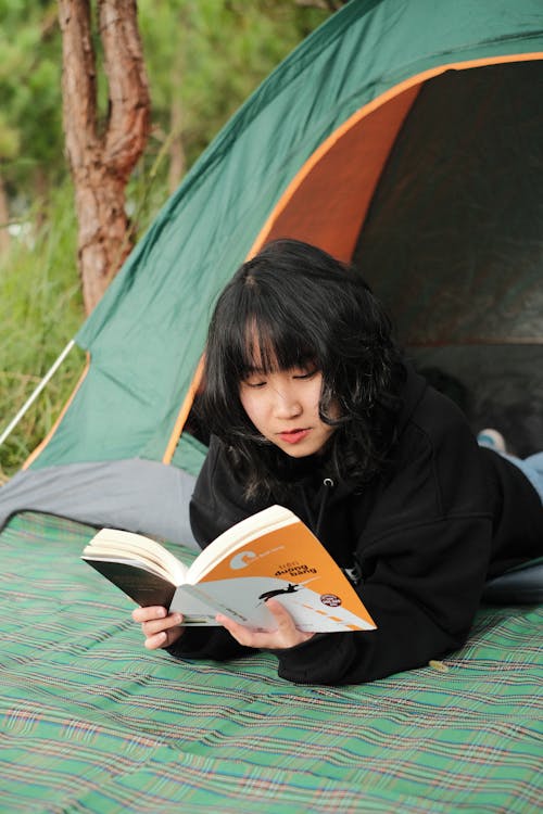 Vertical Shot of Woman Reading a Book outside a Green Tent