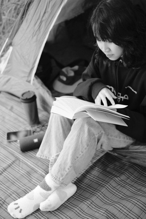 Free Asian woman reading a book inside tent during camping trip, enjoying leisure time. Stock Photo