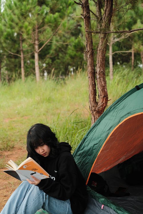 Woman Reading a Book Sitting Near a Green Tent