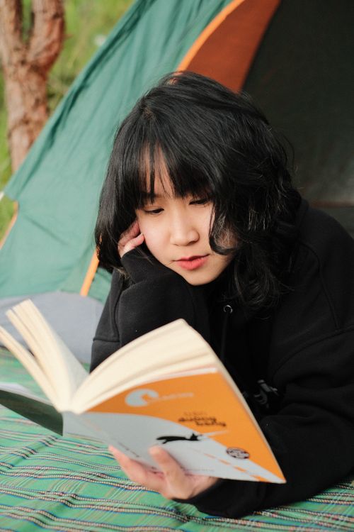 Free A young woman relaxing outdoors, reading a book near a camping tent. Stock Photo
