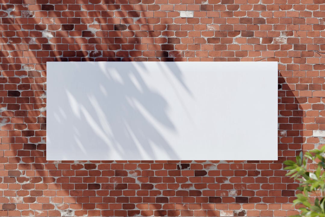 Large blank white banner on a red brick wall with leafy shadows, perfect for mockup designs.