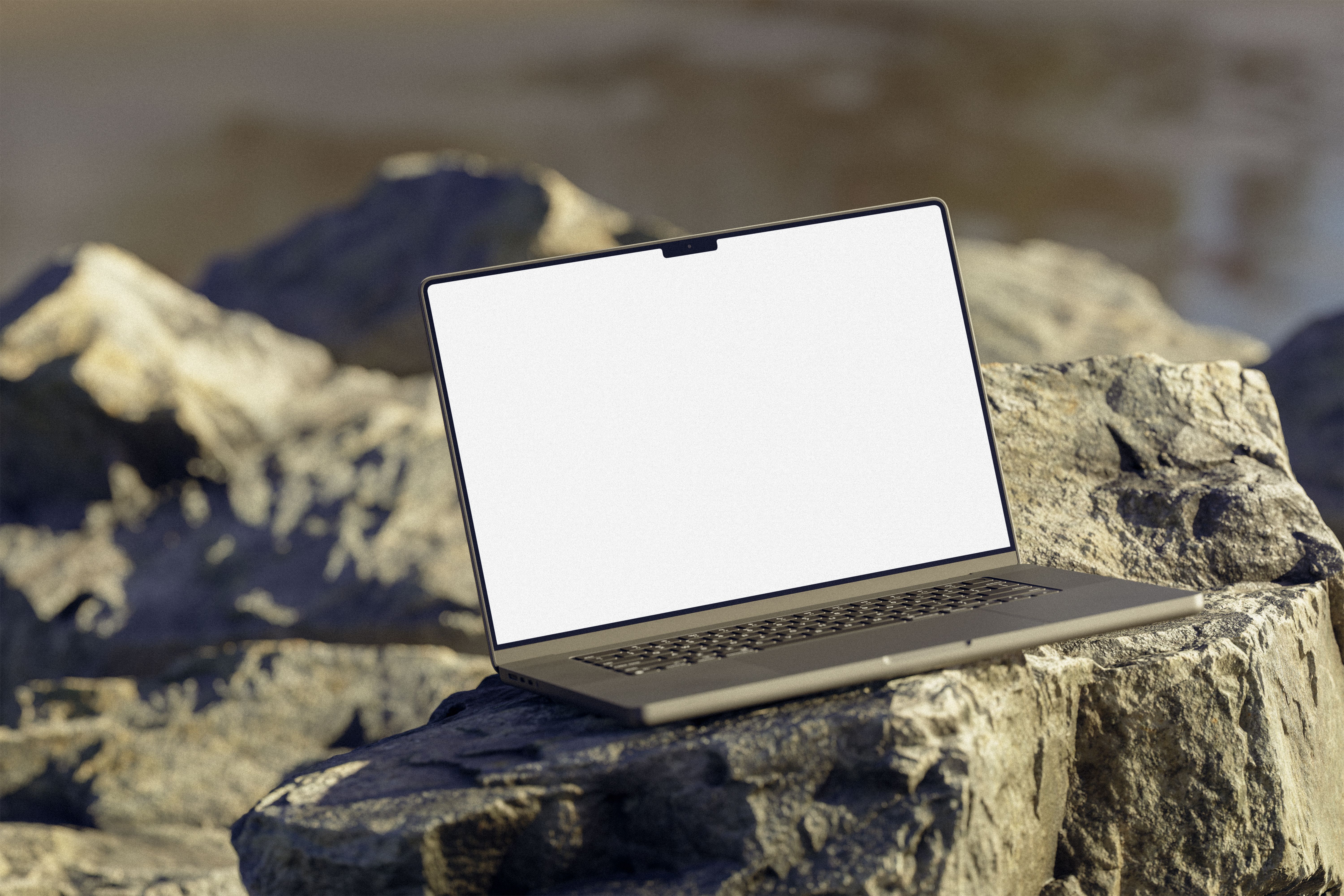 A laptop with a blank white screen rests on rocks outdoors, ideal for mockup and design presentations.