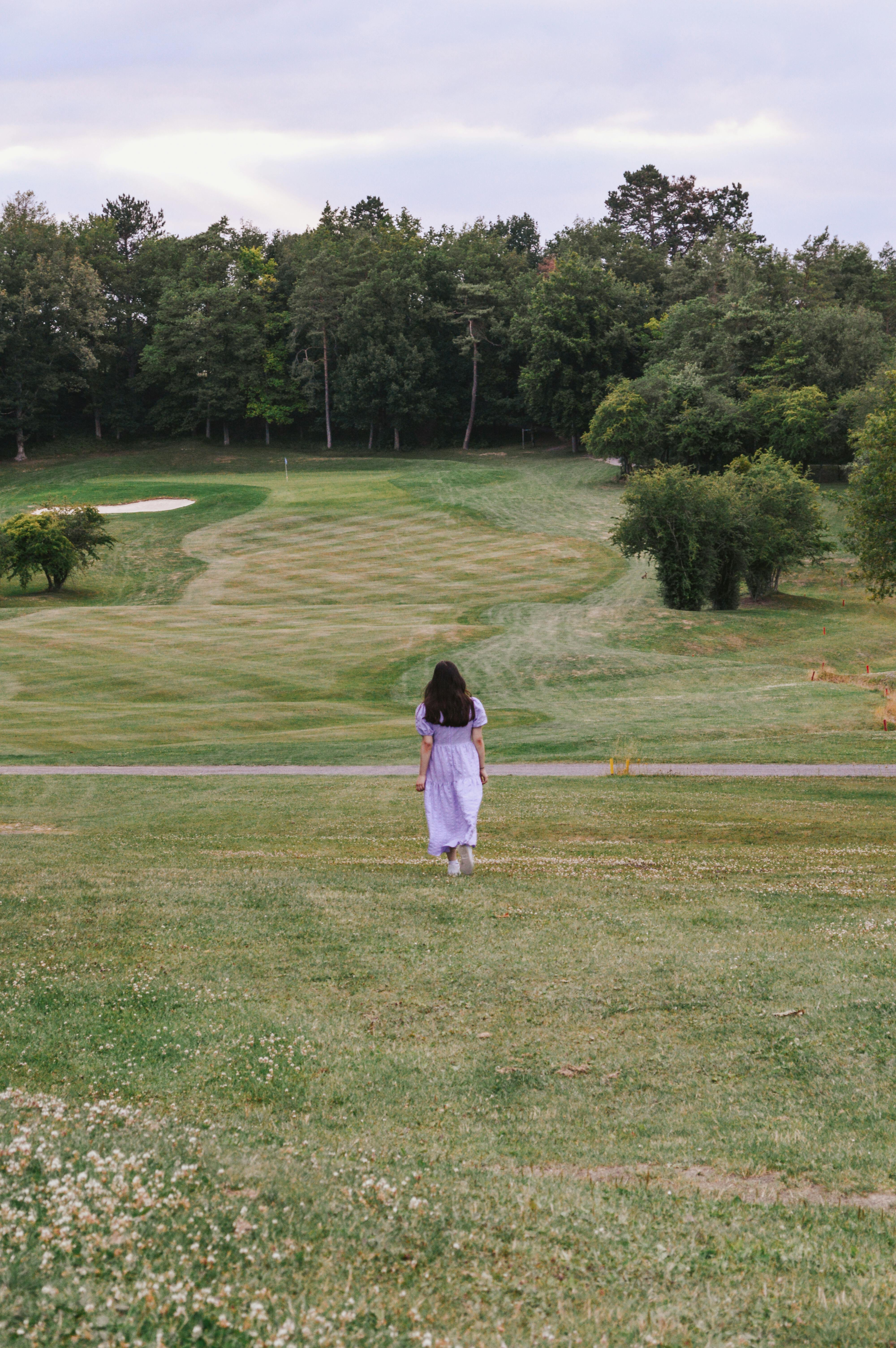 A woman in a purple dress walking on a scenic golf course surrounded by lush greenery.