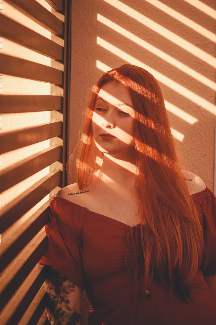 Woman Standing By The Window In The Shade Of Shutters