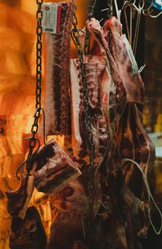 Close-up of raw meat cuts hanging from chains in a butcher shop. Warm lighting adds depth.