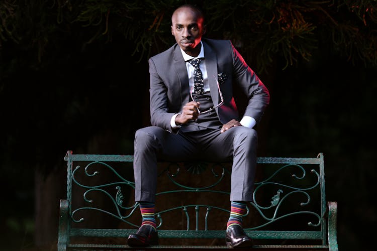 A Man In A Suit Sitting On A Bench 