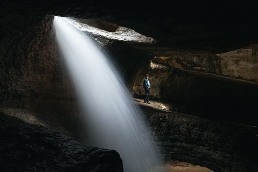 Long exposure of a man standing next to the Saltinskiy waterfall inside a cave in Dagestan, Russia.