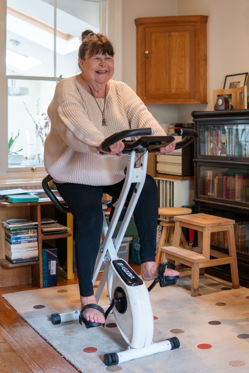 Smiling woman riding a stationary bike at home for low-impact cardio and weight loss