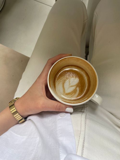 Free Close-up of a hand holding a latte with intricate latte art, viewed from above. Stock Photo