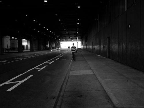 Free A person walking alone in a dark, monochrome city tunnel. Stock Photo
