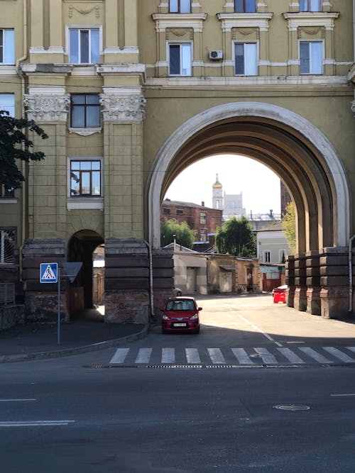 A Red Car Parked Near Brown Concrete Building with Arched Passage