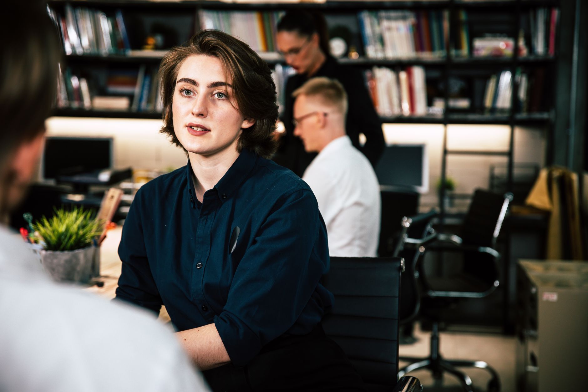 Focused young adult working in a modern office environment. Busy yet calm ambiance with colleagues and workspace.