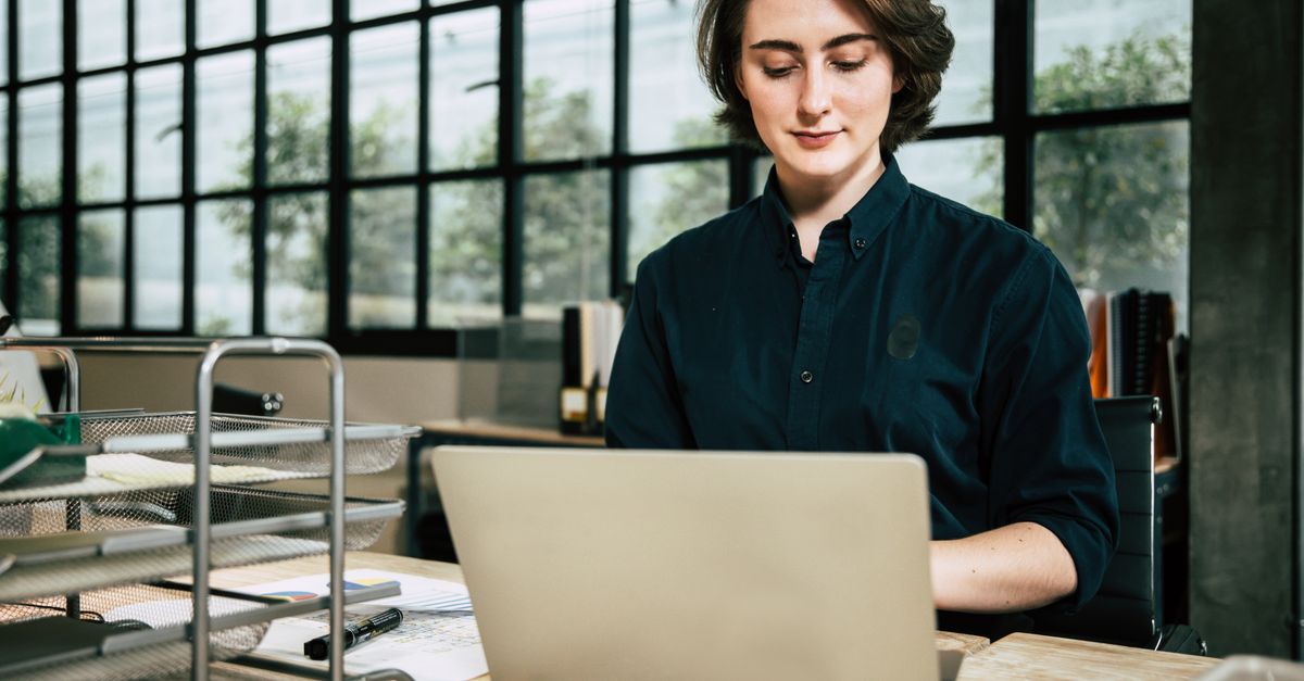 Mulher profissional usando laptop em um ambiente de escritório elegante, focada no trabalho.