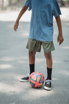 A child in casual outfit playing football outdoors on a sunny day.