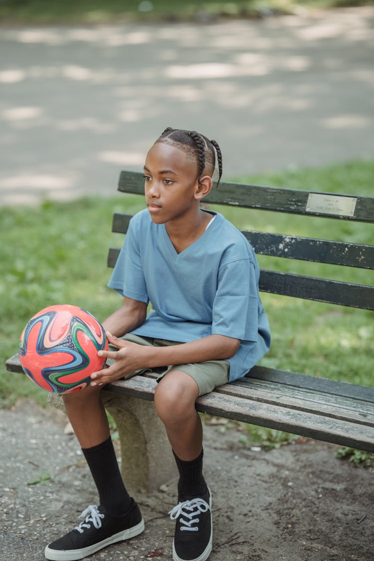 Teenage Boy In Summer Clothing Sitting On Bench In Park