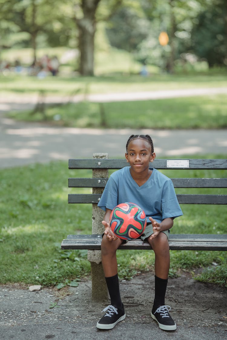 Boy Sitting On A Park Bench Holding A Ball