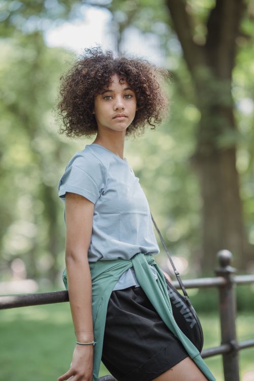 Free Portrait of a teenage girl with natural curly hair leaning on a park railing. Stock Photo