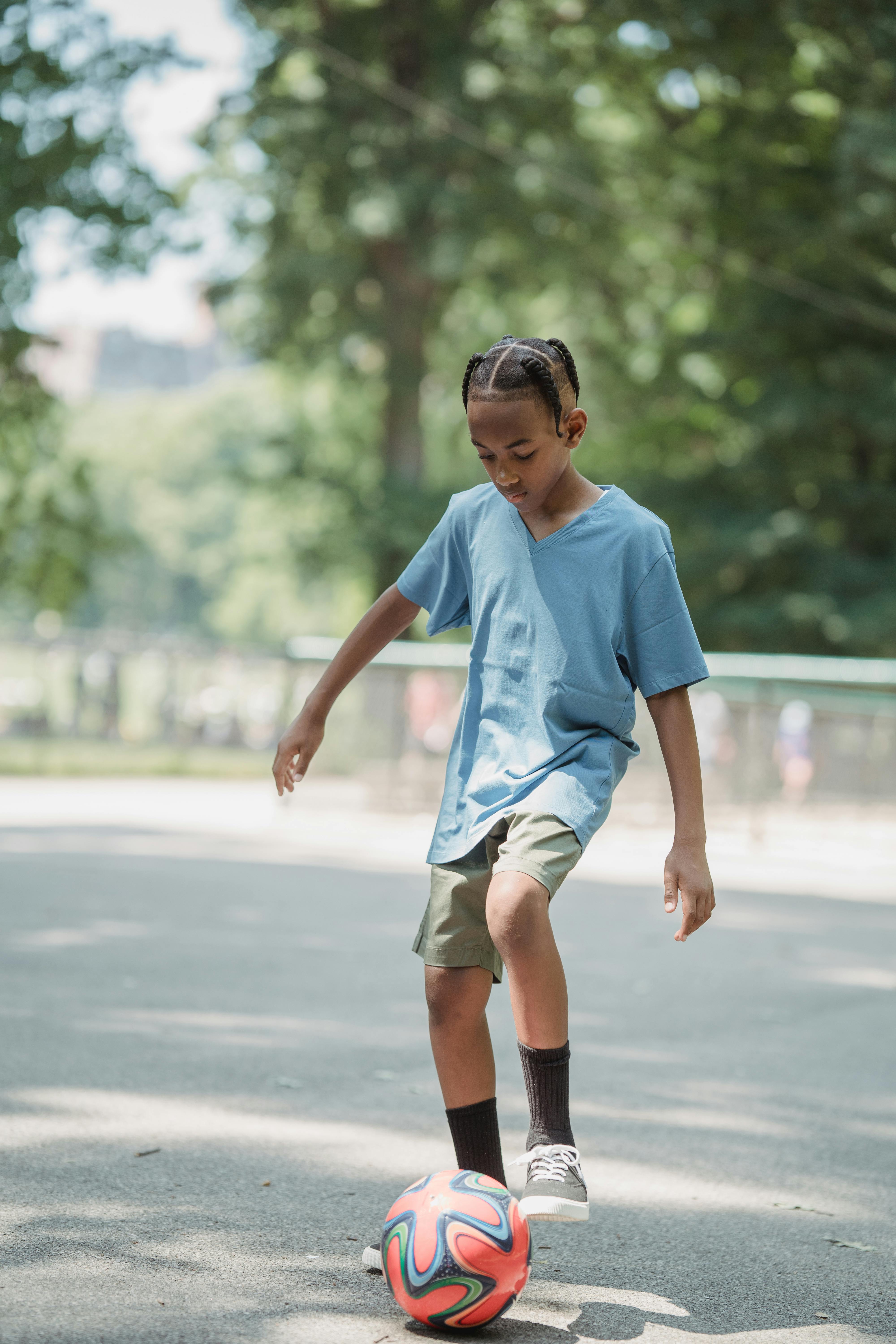 boy kicking a football on asphalt