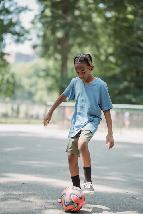 Boy Kicking a Football on Asphalt